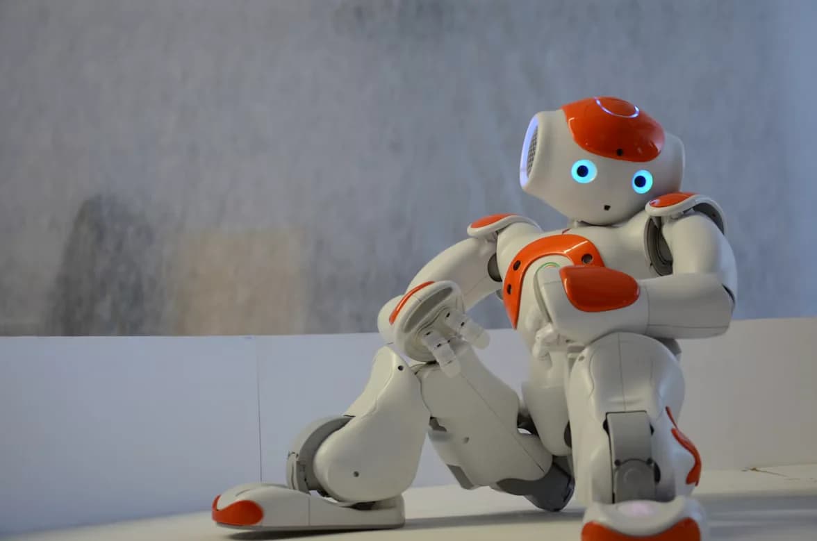 White and orange humanoid robot with glowing blue eyes seated on a bench