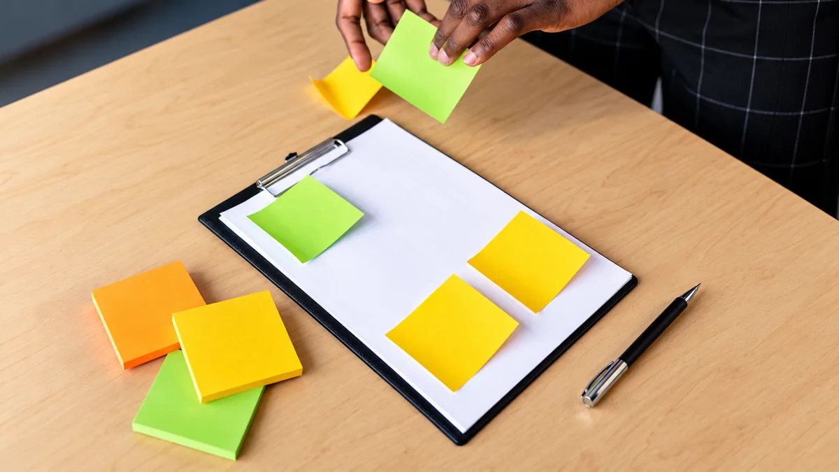 Hands arranging colourful blank sticky notes on a clipboard to organise content ideas